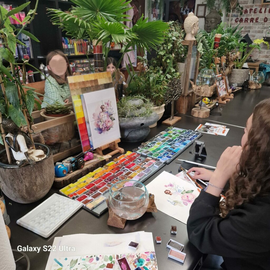 Participante travaillant à l’aquarelle d’après un modèle floral, avec plusieurs palettes de couleurs devant elle.