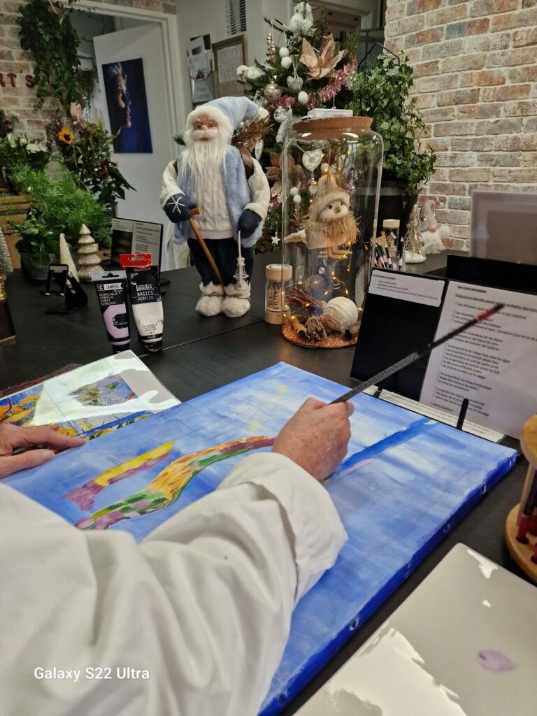 Isabelle peint au pinceau une composition multicolore sur fond bleu, devant les décorations de Noël.